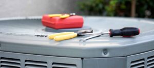 Screwdrivers, a red toolbox, and other repair tools arranged on an outdoor air conditioning unit during maintenance service.