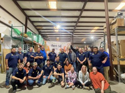 Large group of Southern Air employees wearing blue company shirts posing together in a warehouse with a Happy Fall banner in the background.