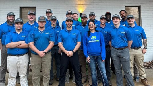 Professional HVAC and electrical service team in blue uniforms posing together in front of brick building.